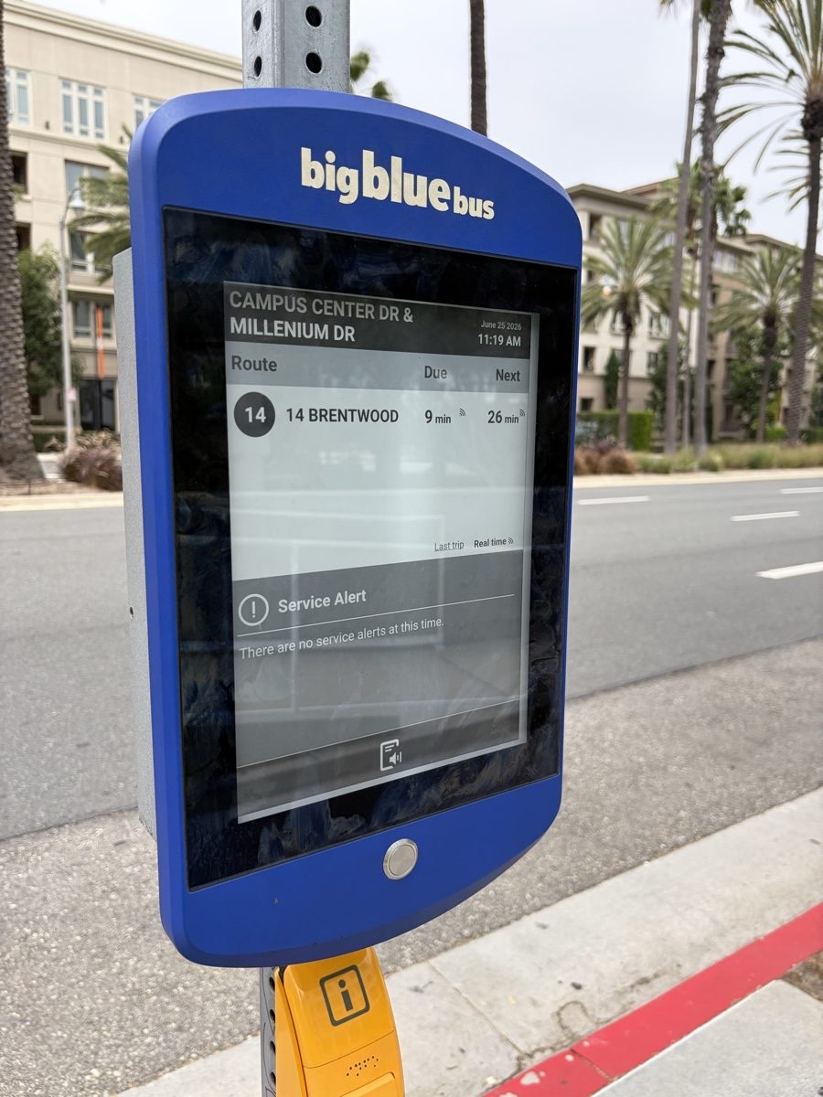 Close-up of a Big Blue Bus solar e-paper display showing the stop name, Route 14 arrival times in minutes and a service alert panel.