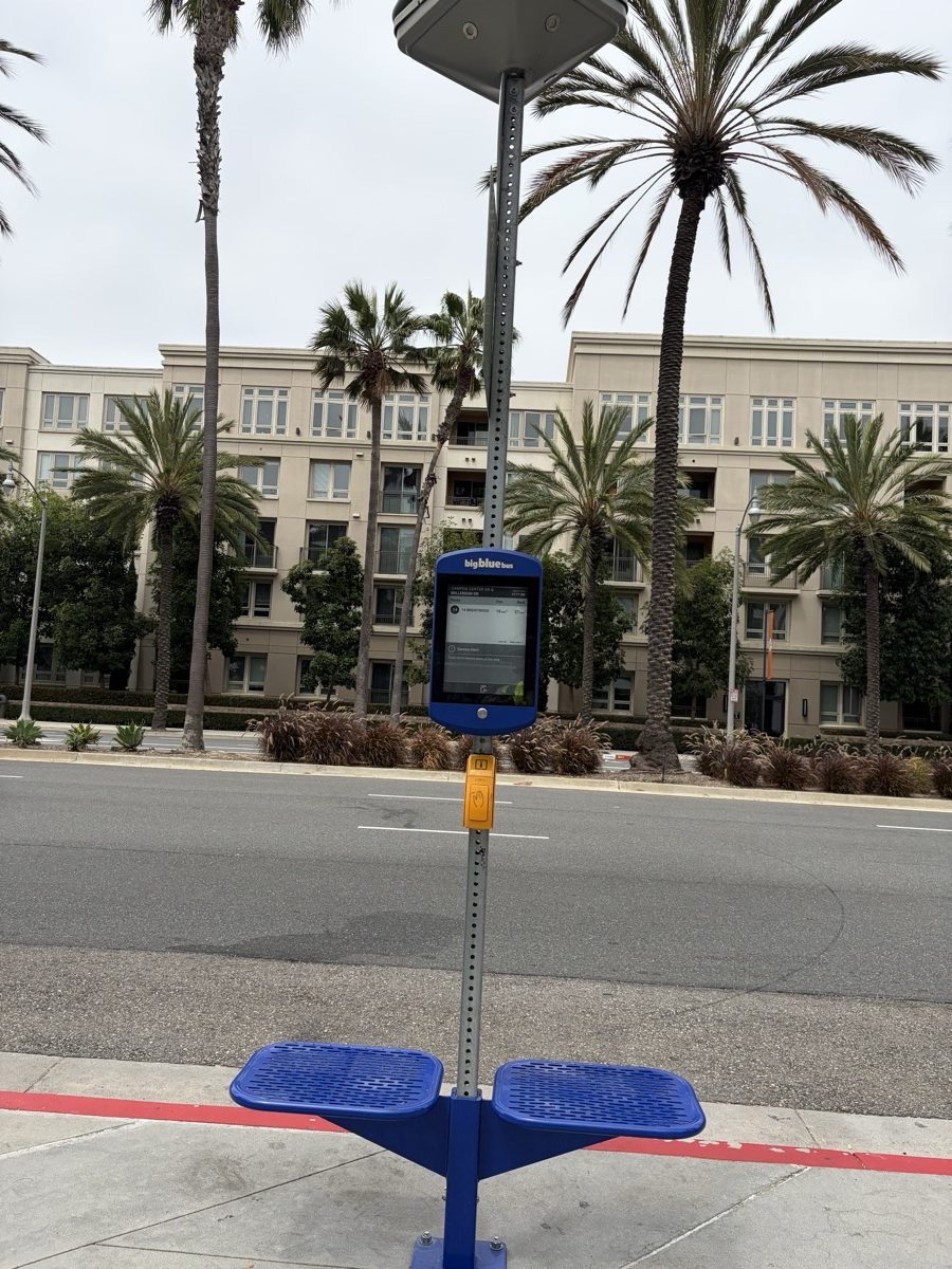 Big Blue Bus stop in Santa Monica with a solar panel on top of the pole, a blue-framed e-paper arrival display and a yellow audio button above a blue bench.
